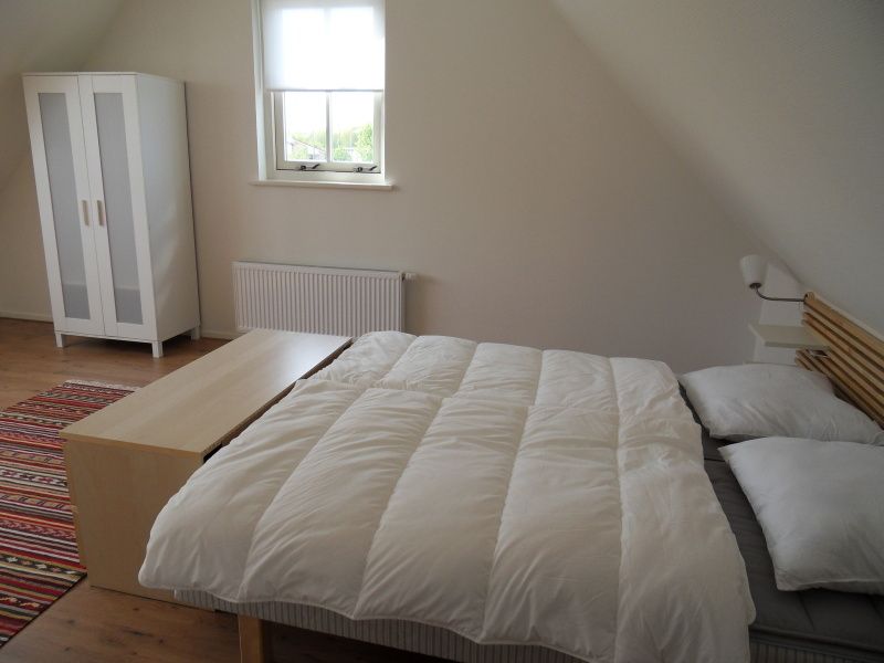 Geraeumiges Schlafzimmer in Typ 7 - 2107 Ferienhaus De Cocksdorp Texel mit bequemem Doppelbett und Holzboden.