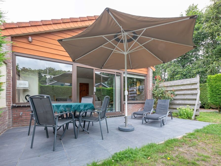 Geniessen Sie die Terrasse des Ferienhauses Slufterhoek 102 in De Cocksdorp, Texel, mit bequemen Stuehlen und einem grossen Sonnenschirm.