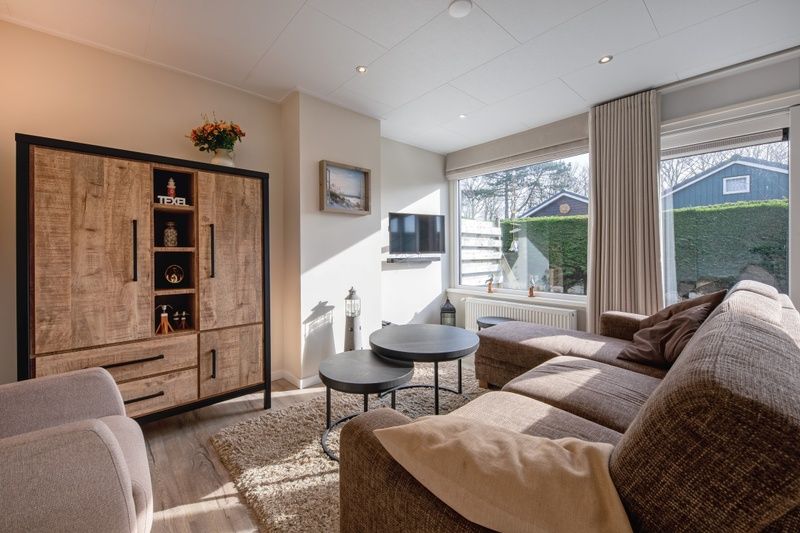 Entspannen Sie sich im gemuetlichen Wohnzimmer des Ferienhauses Slufterhoek 102, De Cocksdorp, Texel mit einem grossen Sofa und viel Tageslicht.