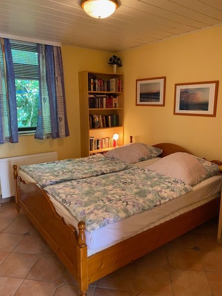 Schlafzimmer im Ferienhaus Slufterhoek 128, De Cocksdorp Texel, mit Doppelbett und Buecherregal.