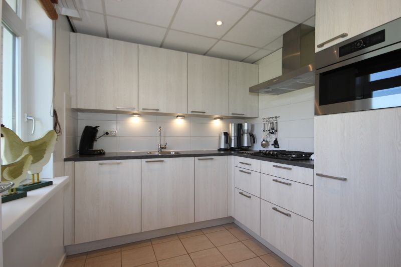Moderne keuken in Bungalow De Witte Hoek 6 Pers., De Cocksdorp, Texel met strakke witte kastjes en inbouwapparatuur.