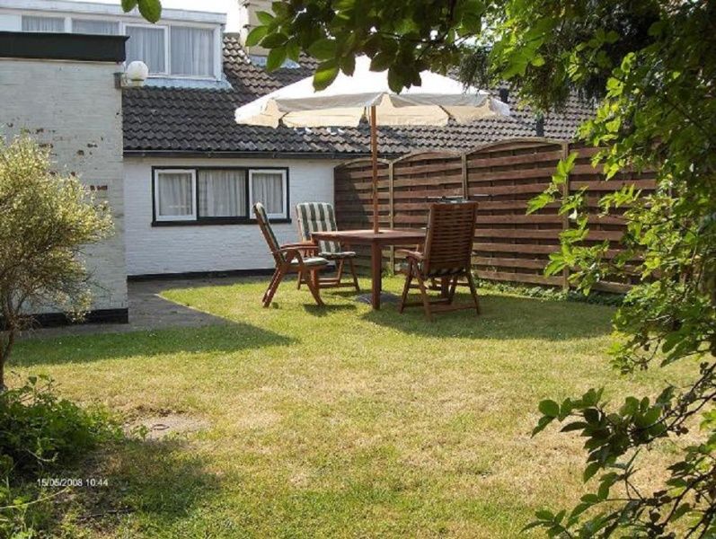 Sunny terrace in the garden of Kikkertstraat 067, De Cocksdorp, Texel, with parasol and seating.