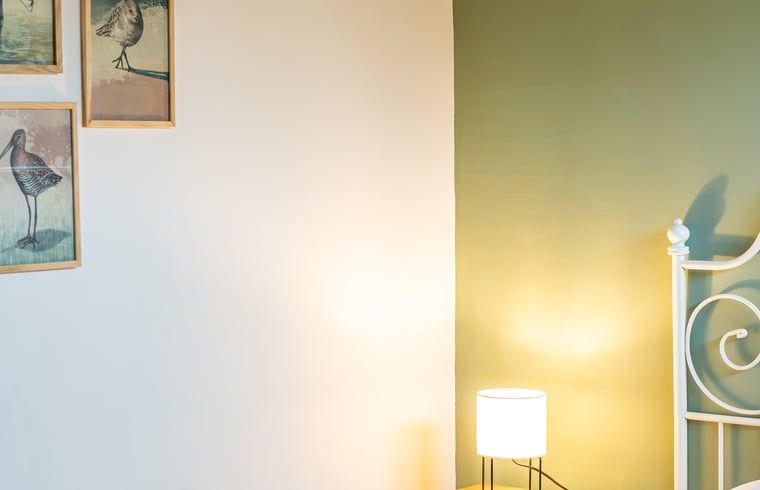 Sfeervolle slaapkamer in Huisje in De Cocksdorp, Texel, met kunst aan de muur en zacht licht.