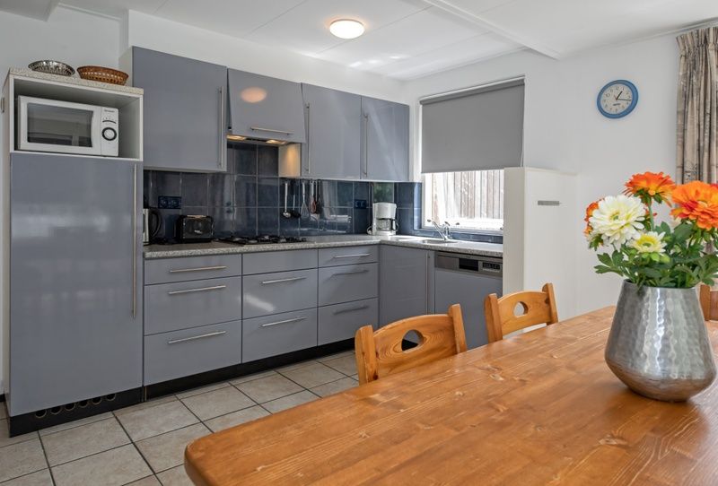 Kueche und Essbereich des Ferienhauses Slufterduin 098, Texel, mit Blumen auf dem Tisch und Zugang zur Terrasse.