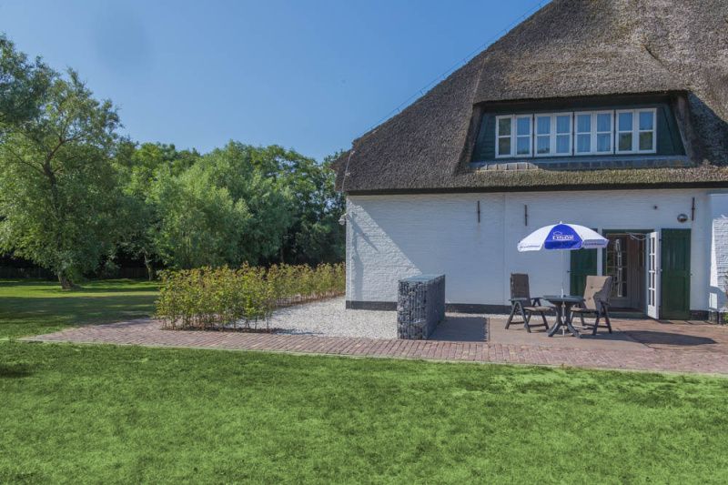 Terrasse mit Sonnenschirm im Ferienhaus Typ R, De Cocksdorp, Texel, ideal fuer entspannte Mahlzeiten im Freien.