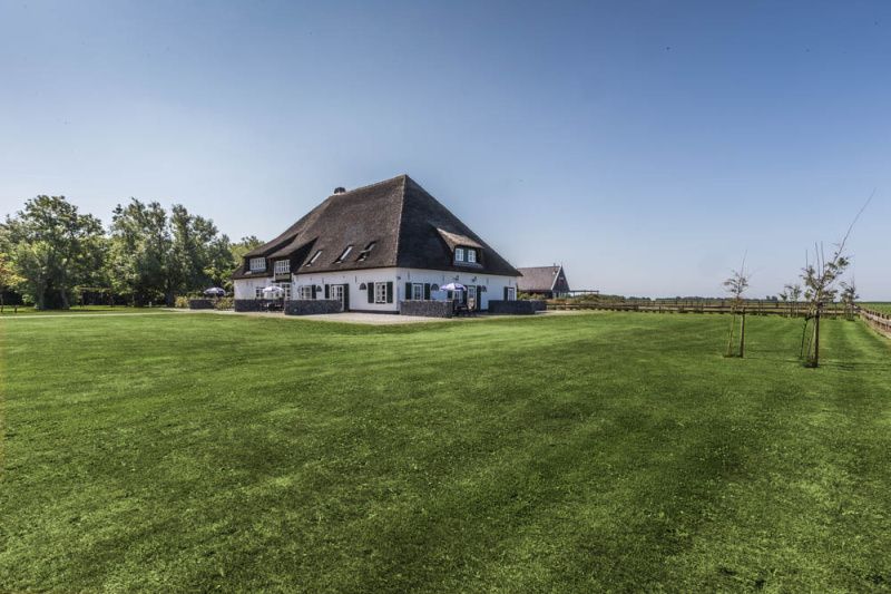 Blick auf das Gelaende des Ferienhauses Typ R, De Cocksdorp, Texel, mit weiten gruenen Feldern.