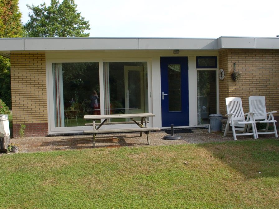 Gemuetliche Terrasse des Bungalows Tamarisk 212 in De Cocksdorp, Texel, mit Sitzgelegenheiten im Garten und gruener Umgebung.