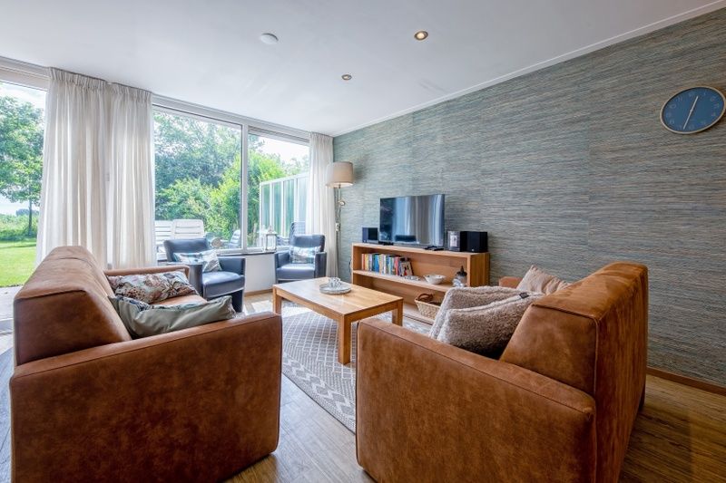Gemuetliches Wohnzimmer im Ferienhaus Slufterhoek 132, De Cocksdorp, Texel, mit bequemen Sofas und Blick auf den Garten