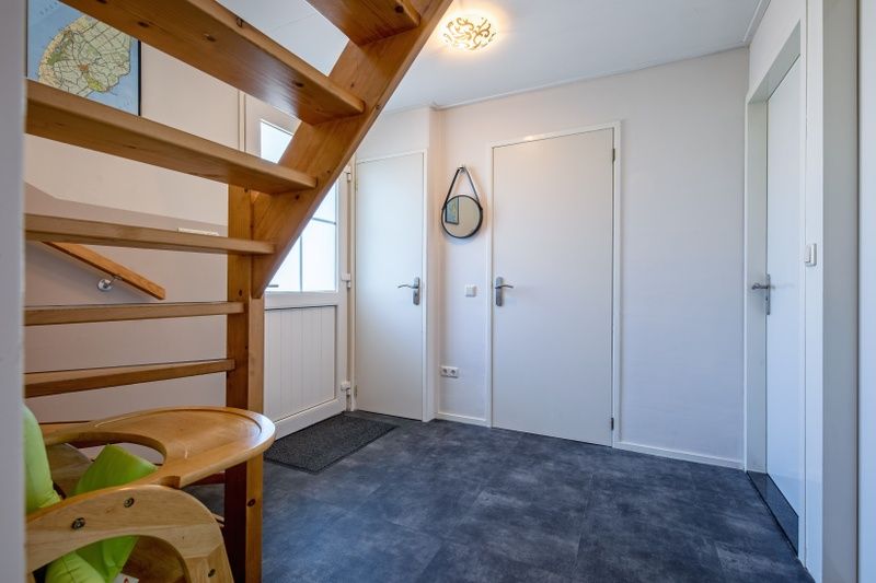 Eingangshalle des Ferienhauses Slufterhoek 132, Texel, mit Holztreppe und stilvollem Mobiliar