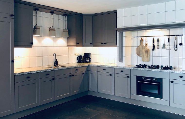 Moderne Kueche im Ferienhaus in De Cocksdorp, Texel, mit grauen Schraenken und kompletten Geraeten.