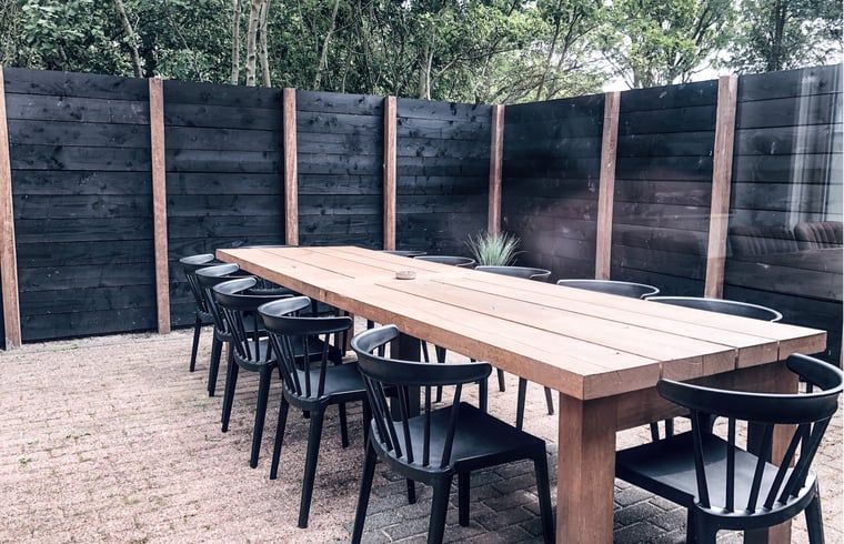 Essbereich im Freien im Ferienhaus in De Cocksdorp, Texel, mit langem Holztisch und schwarzen Stuehlen.
