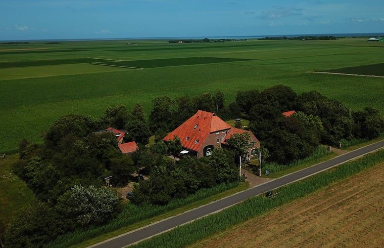 Luftaufnahme des Ferienhauses in De Cocksdorp, Texel, umgeben von gruenen Feldern und natuerlicher Schoenheit auf den Waddeninseln.