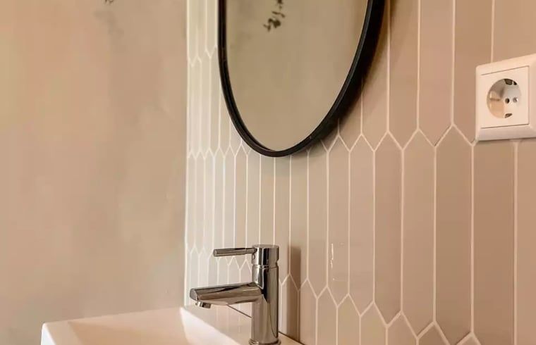 Moderne wastafel in Huisje in De Cocksdorp, Texel, met stijlvolle tegelwand en ronde spiegel.