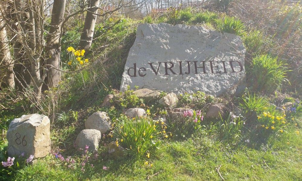 Eingang zum Ferienhaus Paal 86 Texel in De Cocksdorp mit Steinschild und Blumen.