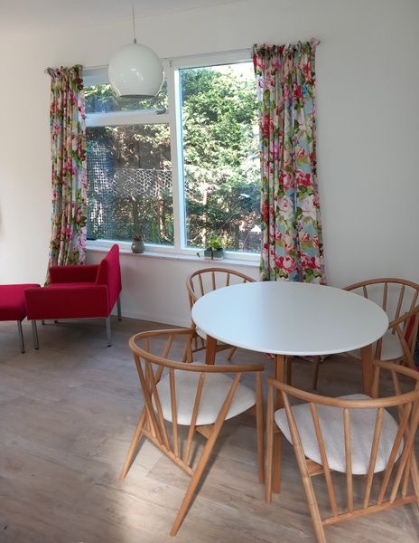 Dining area in Huisje Quirijn, De Koog Texel with round table and wooden chairs surrounded by colorful curtains.
