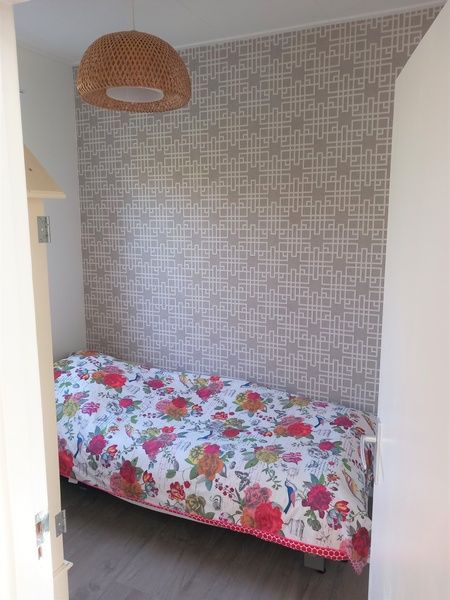 Cozy bedroom in Huisje Quirijn, De Koog Texel with floral pattern comforter and modern wall coverings.