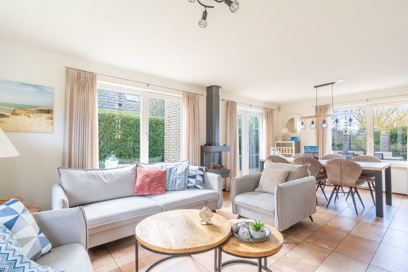 Bright living room of vacation home Honeysuckle 81 in De Koog, Texel with comfortable seating area and garden view, ideal for relaxation.