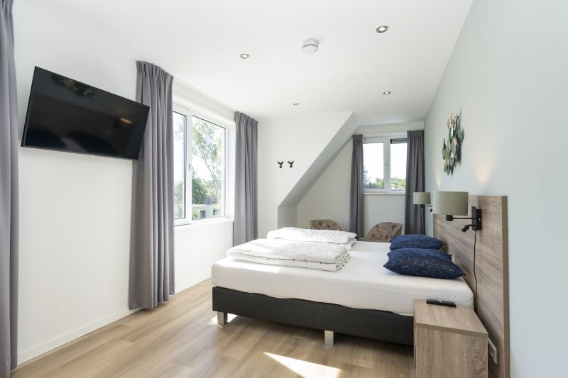 Corner room in Villa 37a, De Koog, Texel, vacation home with large bed and view of green surroundings.