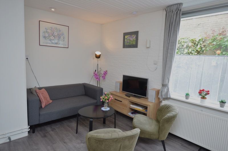 Cozy sitting area in Plevierstraat 18 vacation home, De Koog, Texel with sofa, armchairs and decorative flowers.
