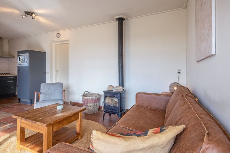 Gemuetliches Wohnzimmer des Ferienhauses De Zonneweelde in De Koog, Texel, mit Holzofen und bequemem Sofa.