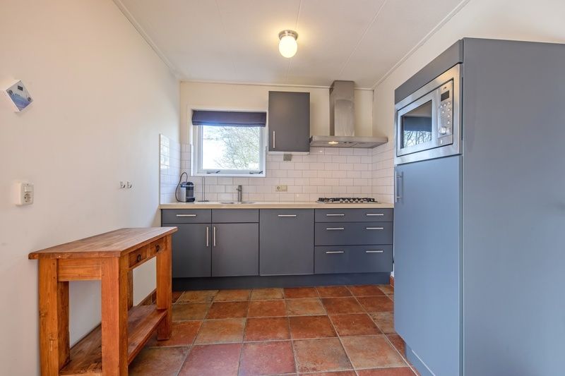 Moderne Kueche von De Zonneweelde in De Koog, Texel, mit schlichten grauen Schraenken und Holzdetails.