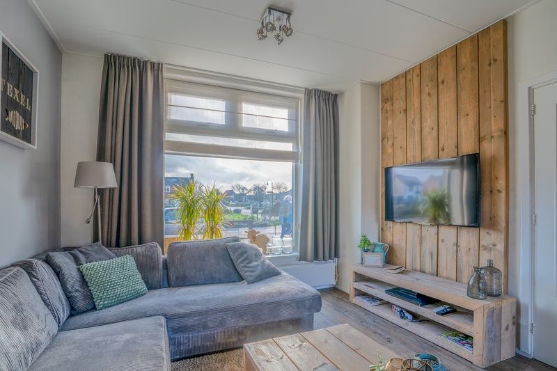 Bright living room of De Bosruiter vacation home in De Koog Texel with a view of the street and a cozy sitting area.