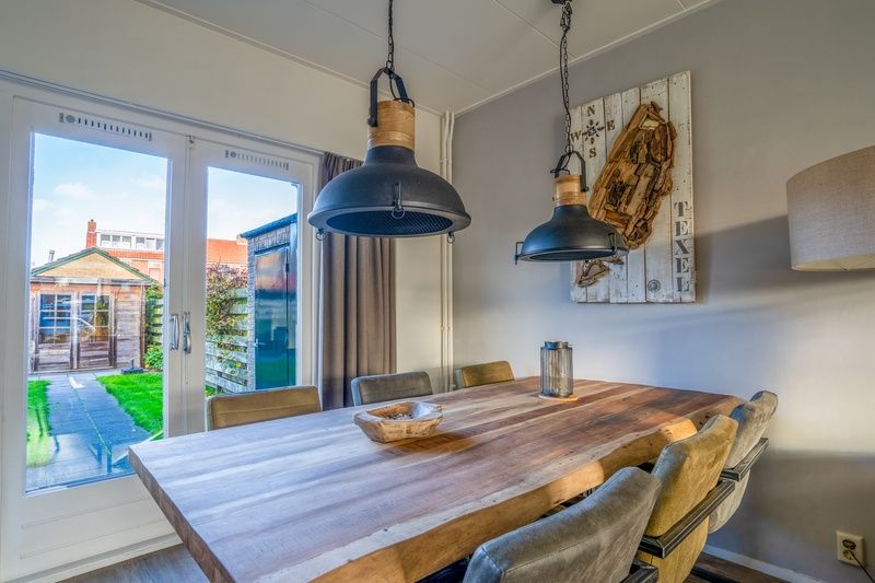 Dining room in De Bosruiter vacation home, De Koog Texel, with wooden table and access to the garden through French doors.