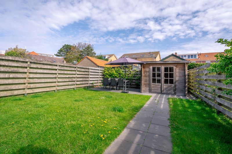 Spacious garden of De Bosruiter vacation home, De Koog Texel, with terrace and wooden gazebo for relaxation.