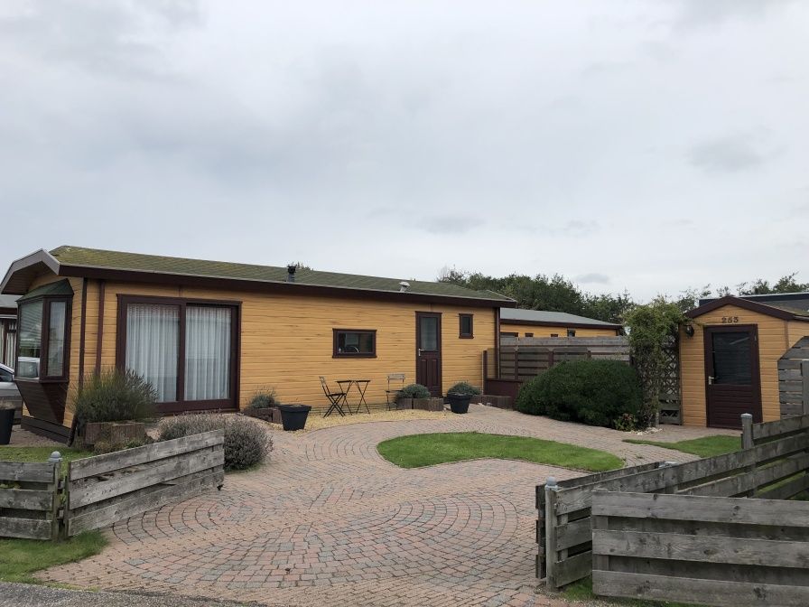 Chaletpark Bregkoog 253 in De Koog, Texel mit charmanter Holzfassade und einladender Terrasse, ideal fuer einen entspannten Urlaub.