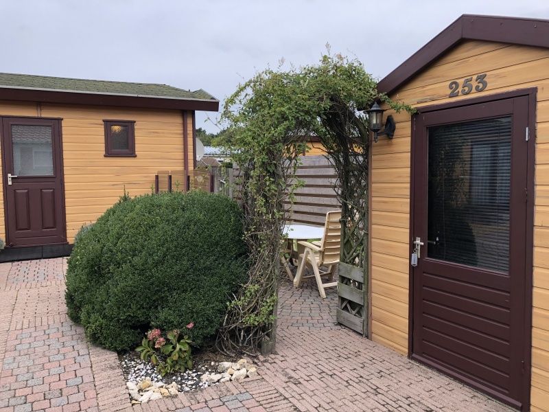 Gemuetliche Terrasse am Chalet Bregkoog 253, De Koog, Texel mit gruenem Zaun und Sitzgelegenheit fuer Mahlzeiten im Freien.