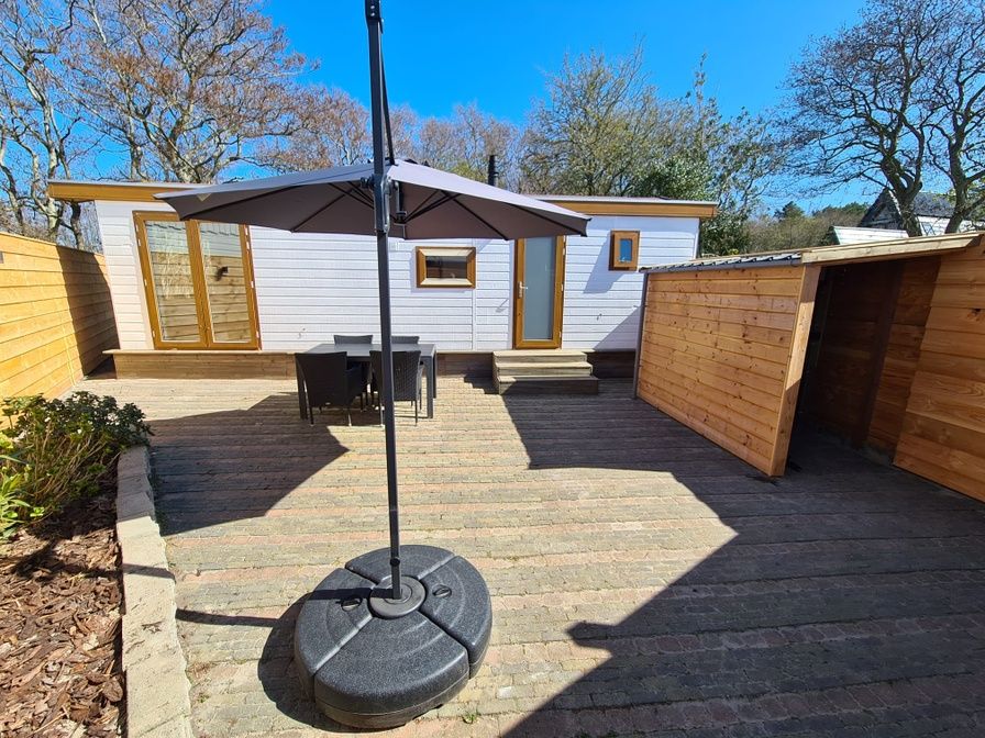 Veranda of Chalet Out and Home in De Koog, Texel, with wooden fence and parasol.