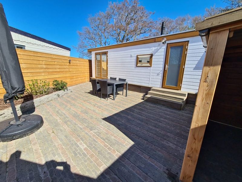 Sunny terrace of Chalet Out and Home in De Koog, Texel, with wooden fence and garden furniture.