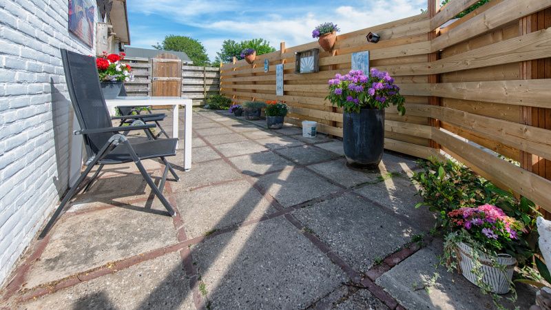 Geraeumige Terrasse am Ferienhaus 2490 in De Koog, Texel, umgeben von einem Holzzaun und bunten Blumen.