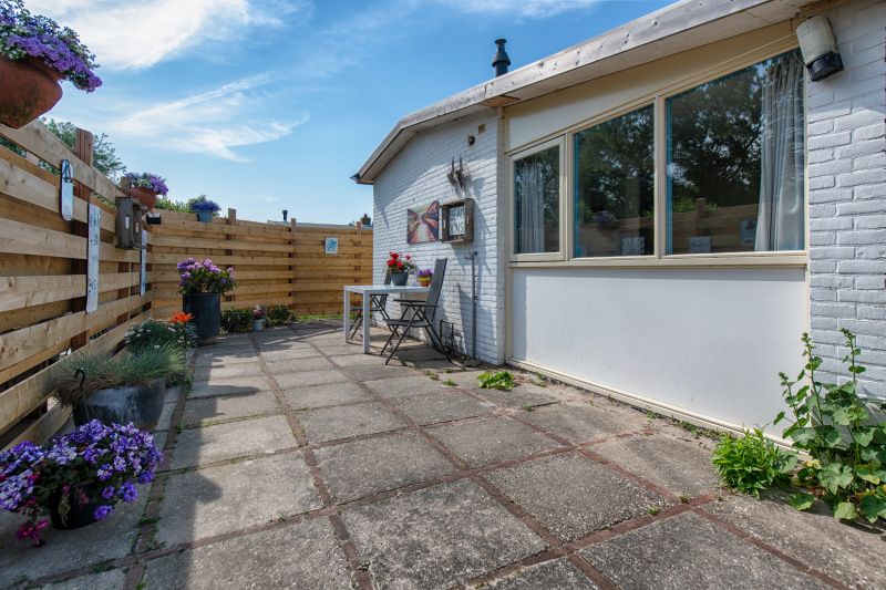 Private Terrasse Ferienhaus 2490, De Koog, Texel, mit Holzzaun und bunten Blumen.