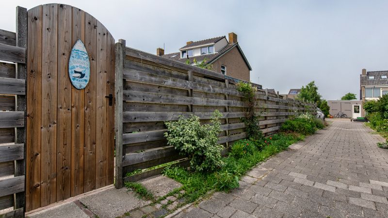 Eingang zum Ferienhaus 2490 in De Koog, Texel, mit Holztor und gruener Umgebung.