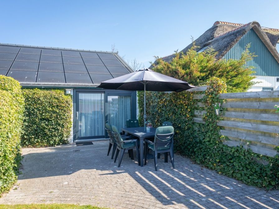 Gemuetliche Terrasse am Bungalow 1 in De Koog, Texel mit Gartenmoebeln und Sonnenschirm fuer ein optimales Leben im Freien.