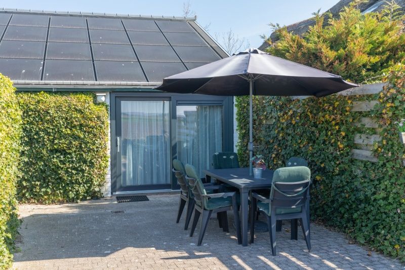 Aussenterrasse von Bungalow 1, De Koog, Texel mit Sonnenschirm und Sitzgelegenheit zum Entspannen.
