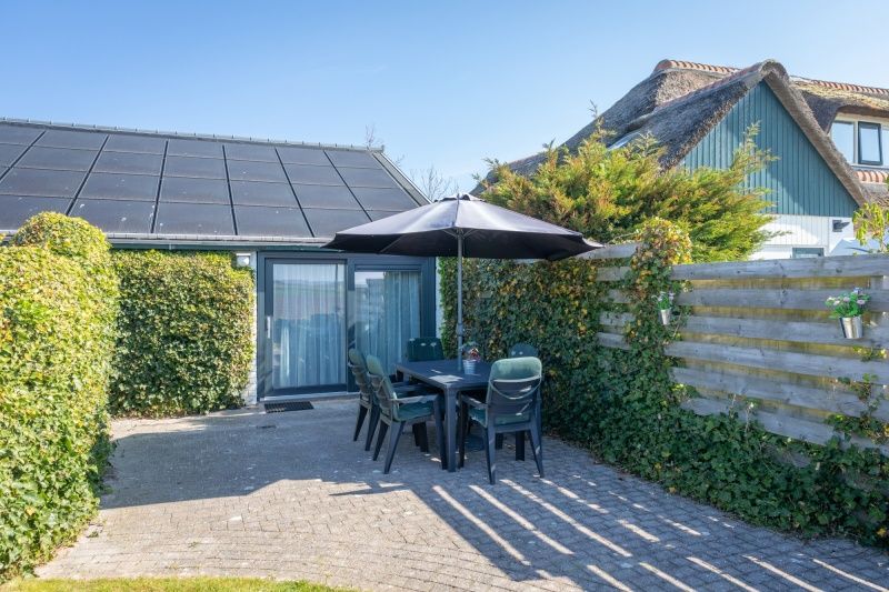 Terrasse am Bungalow 1, De Koog, Texel mit schattigen Sitzplaetzen und gruener Umgebung.