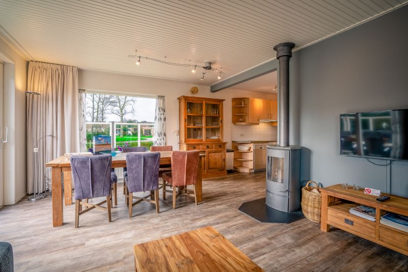 Open kitchen and dining area in Orchismient 2, vacation home De Koog, Texel with wood stove and large windows.