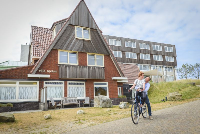 Exterior of Grand Hotel Opduin - Apartment C in De Koog, Texel, with charming architecture and cycling guests.