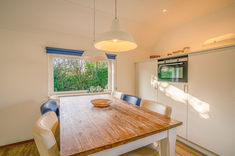 Dining area in Holiday home Honeysuckle 65, De Koog, Texel, with wooden table and garden view.
