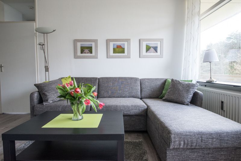 Gemuetliche Sitzecke in 't Kerckeland - Apartment Kerckeland 88, De Koog, Texel mit bequemem Sofa und dekorativen Kunstwerken.