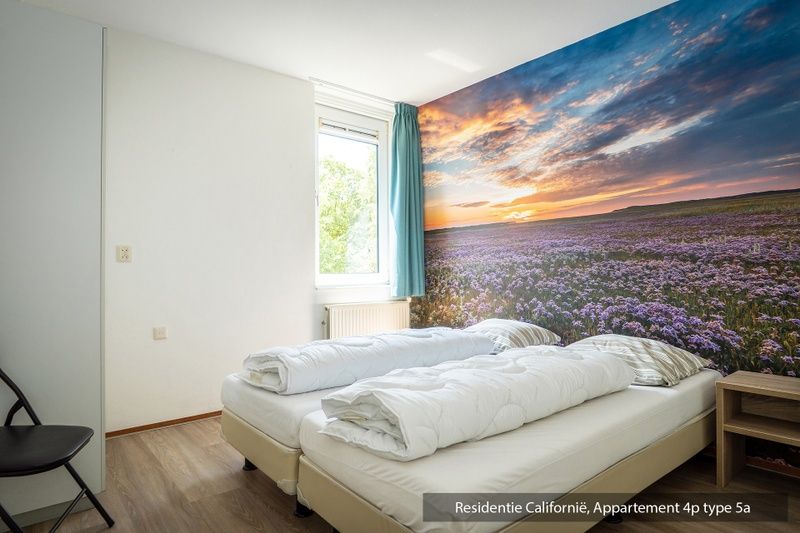 Schlafzimmer in einer Unterkunft des Typs 5A, De Koog, Texel, mit zwei Betten und bunter Landschaftstapete.
