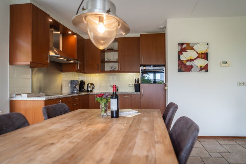 Dining area and kitchen of Villa 304 in De Koog, Texel with stylish wooden table for cozy meals.