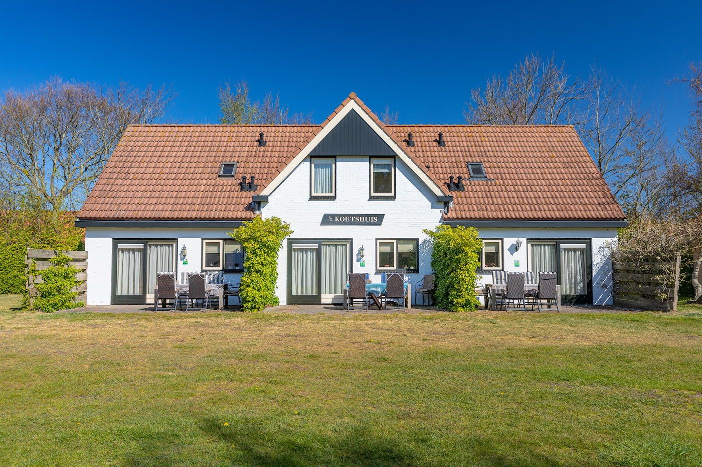 Front view of Koetshuis 3 vacation home in De Koog, Texel with terrace and green surroundings.