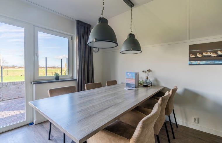 Esszimmer im Ferienhaus in De Waal, Texel mit modernen Pendelleuchten und Blick auf die gruene Landschaft.