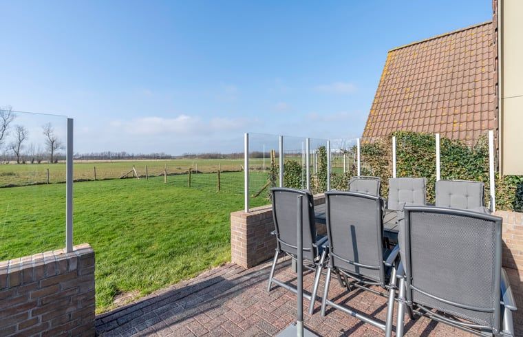 Geraeumige Terrasse im Ferienhaus in De Waal, Texel mit Gartenmoebeln und Blick auf die weite Landschaft.
