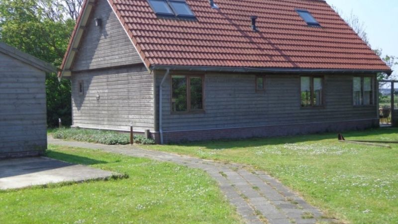 Seitenansicht des Ferienhauses Duinzicht in Den Burg Texel mit roten Dachziegeln und Rasen.