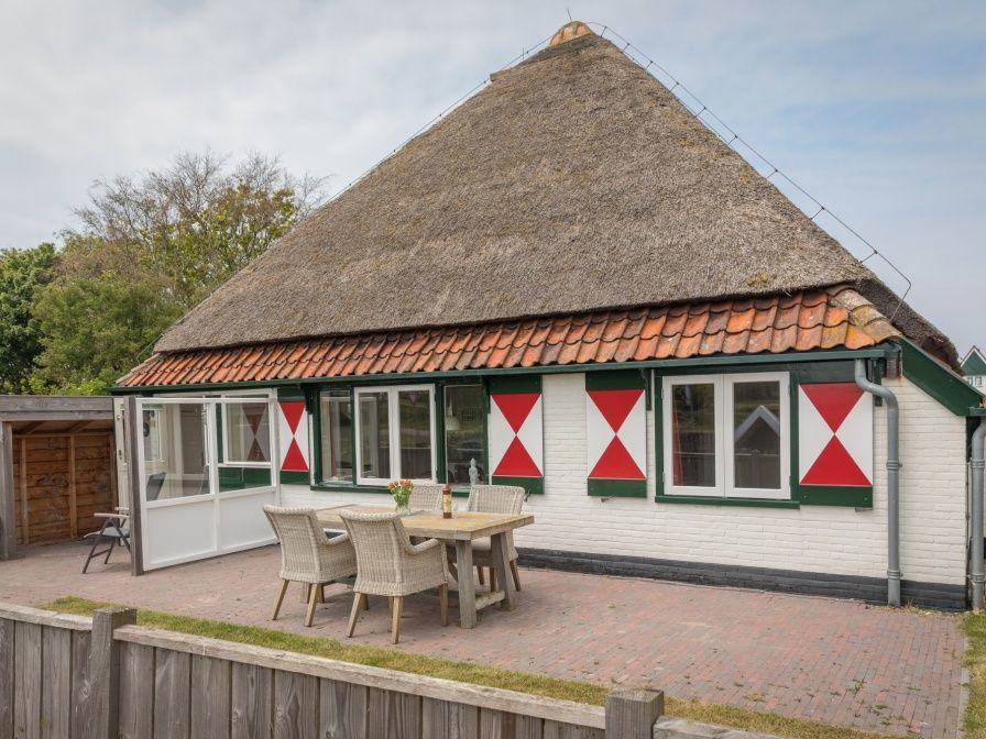 Buitenzicht van Appartement Heem, een charmante vakantiewoning in Den Hoorn, Texel, met traditioneel rieten dak en gezellige veranda.