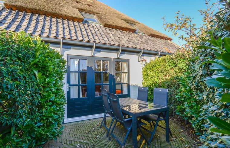 Terrasse des Ferienhauses in Oosterend, Texel, Ferienhaus mit Tisch im Freien, umgeben von Gruen auf den Watteninseln.